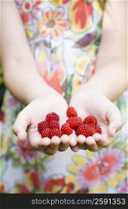 Mid section view of a girl&acute;s hands holding raspberries