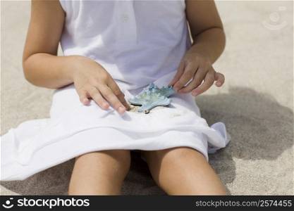 Mid section view of a girl playing with a starfish on the beach