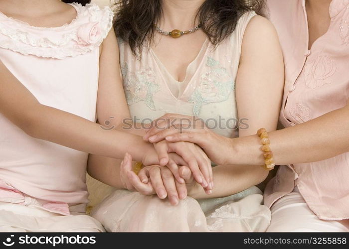Mid section view of a girl with her mother and grandmother stacking their hands