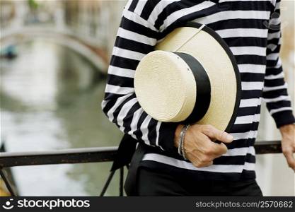 Mid section view of a gondolier standing and holding a hat, Venice, Veneto, Italy