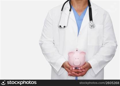 Mid section view of a male doctor holding a piggy bank