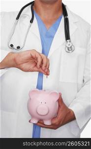 Mid section view of a male doctor inserting a coin into a piggy bank