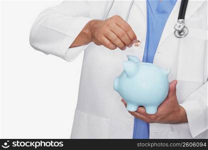 Mid section view of a male doctor inserting a coin into a piggy bank