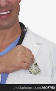 Mid section view of a male doctor putting dollar bills into his pocket