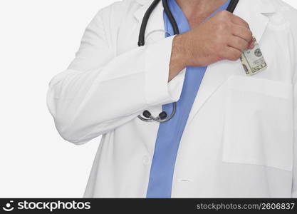 Mid section view of a male doctor putting dollar bills into his pocket