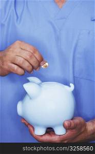 Mid section view of a male nurse inserting a gold coin into a piggy bank