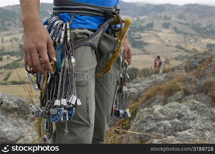 Mid section view of a male rock climber carrying rock climbing equipments