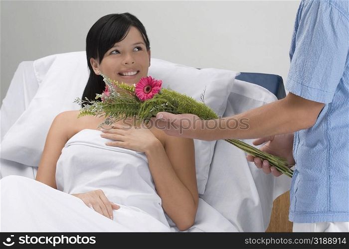 Mid section view of a man giving bouquet of flowers to a patient lying on the bed
