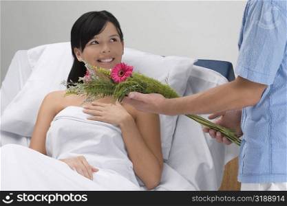Mid section view of a man giving bouquet of flowers to a patient lying on the bed