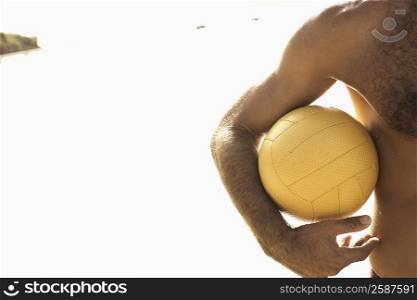 Mid section view of a man holding a beach volleyball on the beach