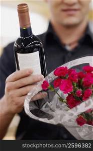 Mid section view of a man holding a bottle of wine and a bouquet of flowers