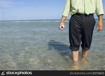 Mid section view of a man holding a flip phone in water