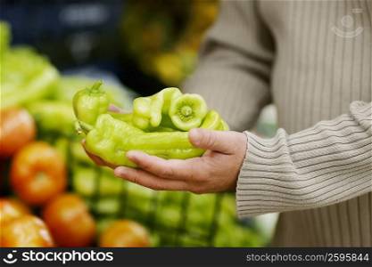 Mid section view of a man holding green bell peppers