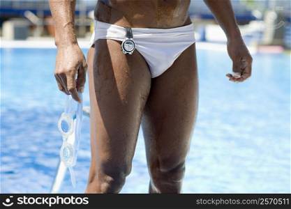 Mid section view of a man holding swimming goggles and standing at the poolside