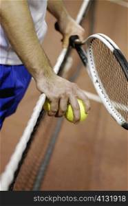 Mid section view of a man holding two tennis balls and a tennis racket