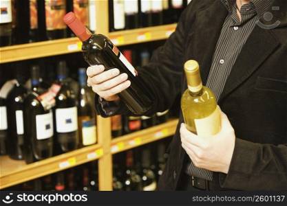 Mid section view of a man holding two wine bottles in a liquor store