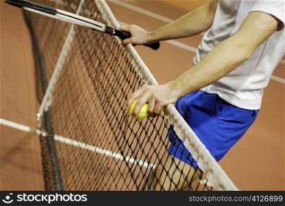 Mid section view of a man leaning against a tennis net
