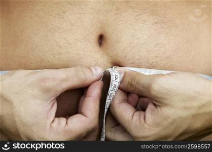 Mid section view of a man measuring his abdomen with a tape measure