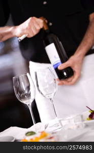 Mid section view of a man opening the cork of a wine bottle