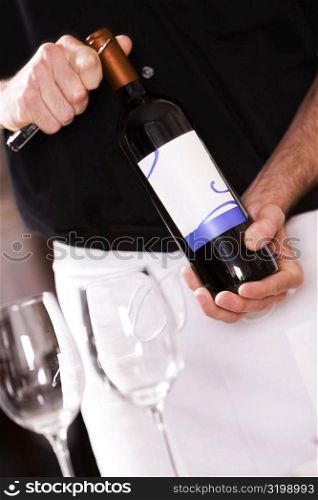 Mid section view of a man opening the cork of a wine bottle