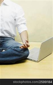 Mid section view of a man performing yoga with a laptop beside him