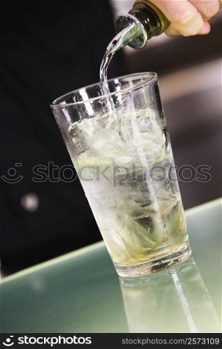Mid section view of a man pouring alcohol into a glass filled with ice