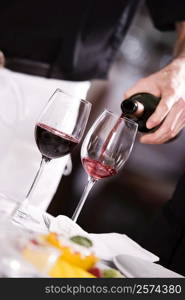 Mid section view of a man pouring red wine into a wineglass