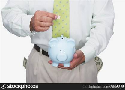 Mid section view of a man putting a coin into a piggy bank