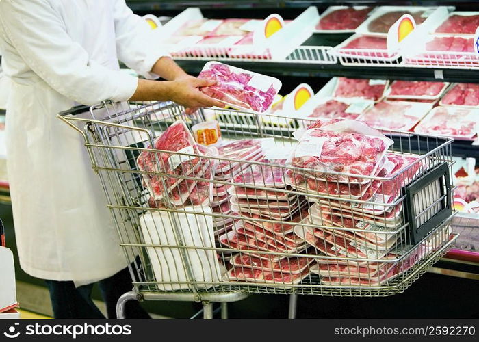 Mid section view of a man putting packaged meat in a shopping cart