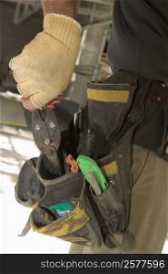 Mid section view of a man putting pliers into a tool belt