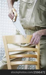 Mid section view of a man sawing a chair
