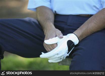Mid section view of a man sitting on the bench wearing a golf glove