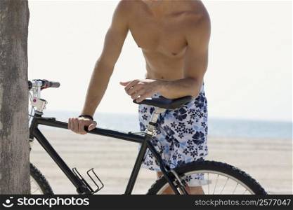 Mid section view of a man standing and holding a bicycle on the beach
