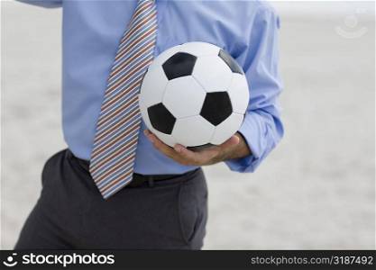 Mid section view of a man standing on the beach and holding a soccer ball