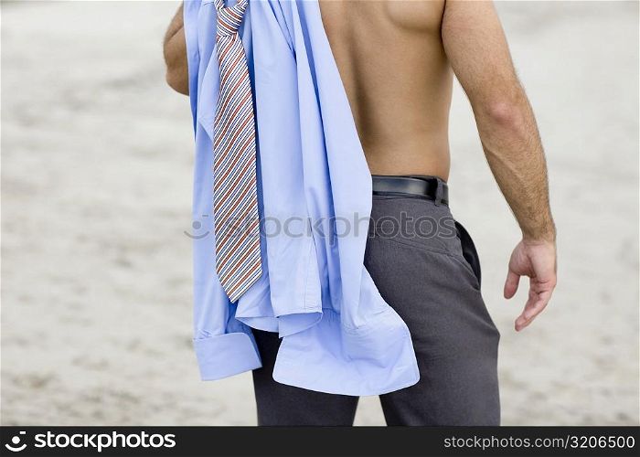 Mid section view of a man standing on the beach with a shirt and tie on his shoulder