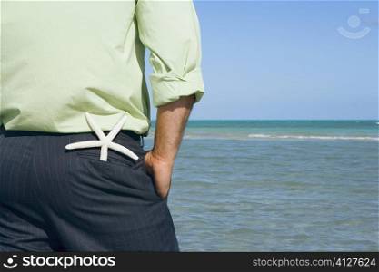Mid section view of a man standing on the beach with his hands in his pockets