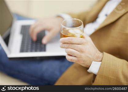 Mid section view of a man using a laptop and holding a glass of wine
