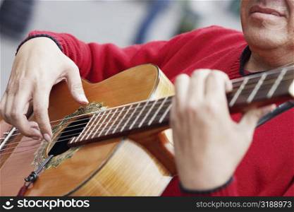 Mid section view of a mature man playing an acoustic guitar