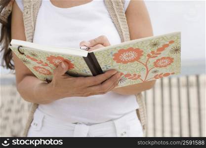 Mid section view of a mature woman writing on a book with a pen