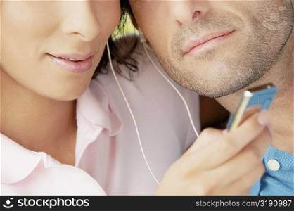 Mid section view of a mid adult couple listening an MP3 player