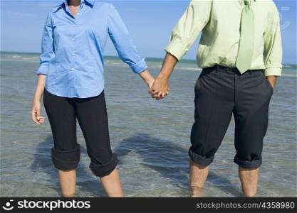 Mid section view of a mid adult couple standing on the beach with holding their hands
