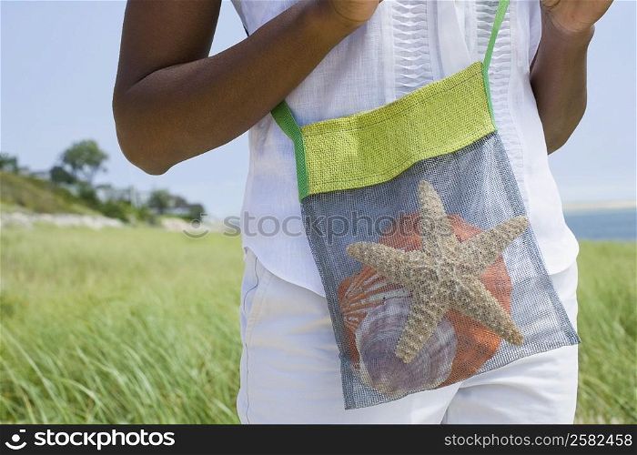 Mid section view of a mid adult woman holding starfish and shells in a bag