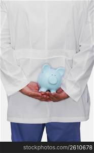 Mid section view of a person holding a piggy bank behind his back