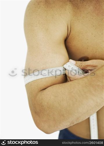 Mid section view of a person measuring his bicep with a tape measure