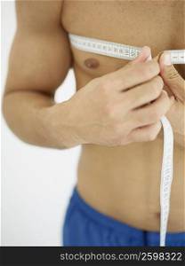 Mid section view of a person measuring his chest with a tape measure