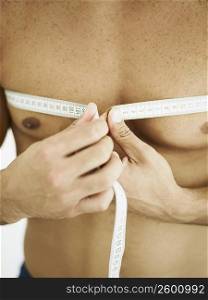 Mid section view of a person measuring his chest with a tape measure