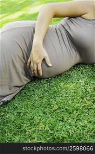 Mid section view of a pregnant woman lying on the grass and touching her abdomen