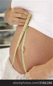 Mid section view of a pregnant woman measuring her abdomen with a measuring tape
