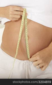 Mid section view of a pregnant woman measuring her abdomen with a measuring tape