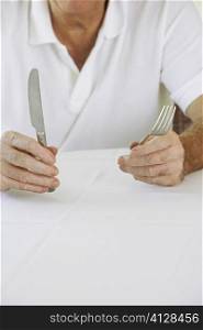 Mid section view of a senior man holding a table knife and a fork